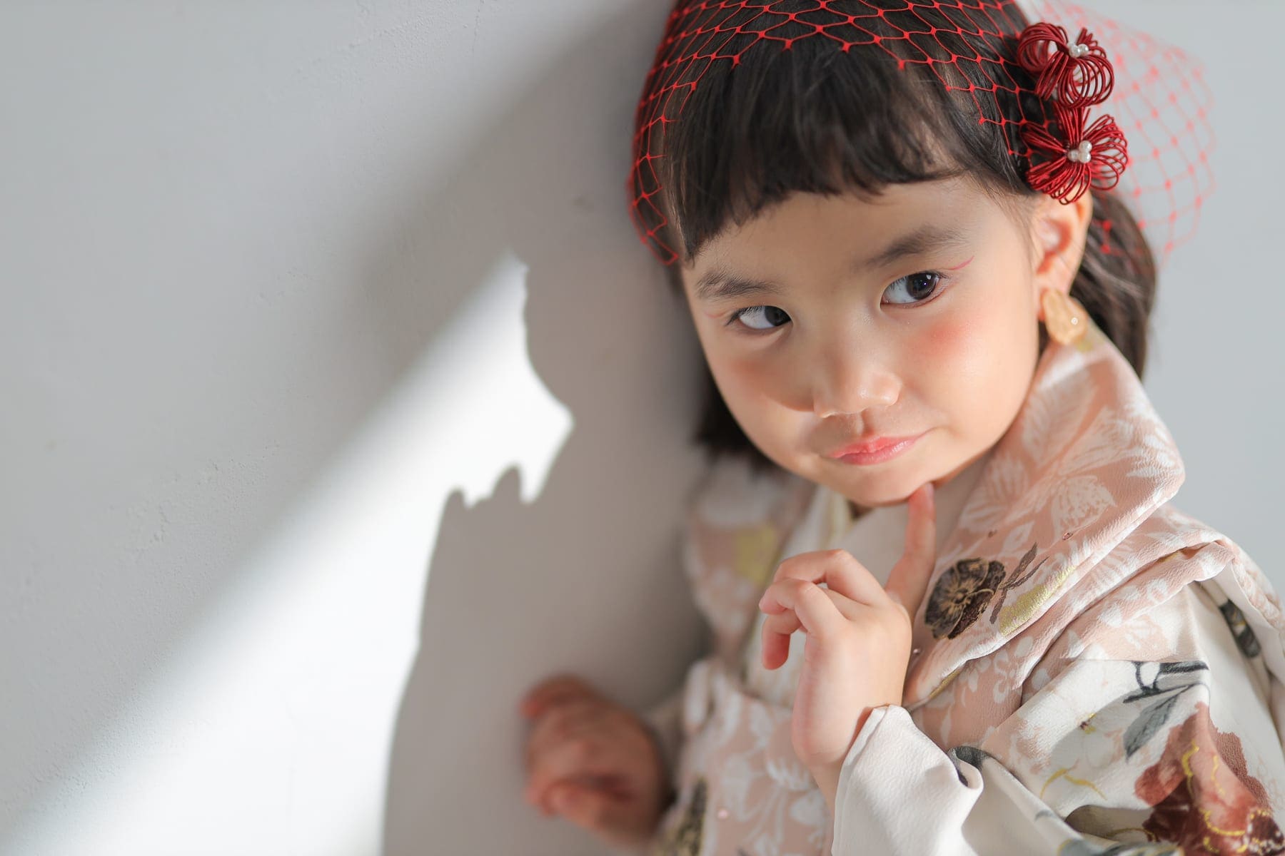 赤い髪飾りをつけ、着物姿で壁にもたれる女の子