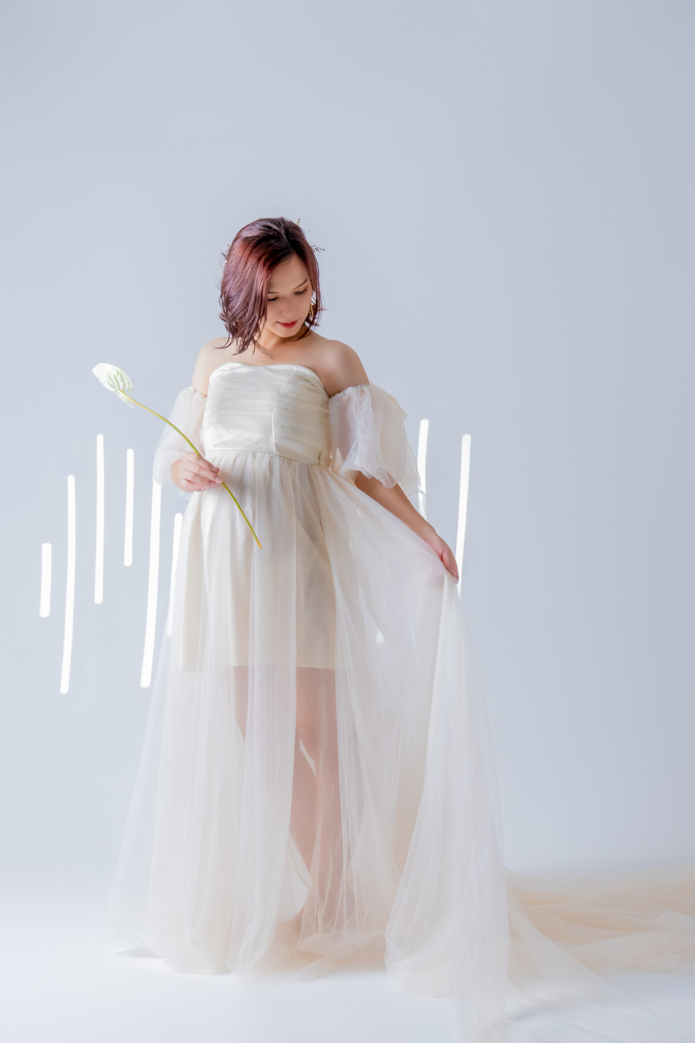 白いマタニティドレスをまとい、明るい光の中に立つ姿