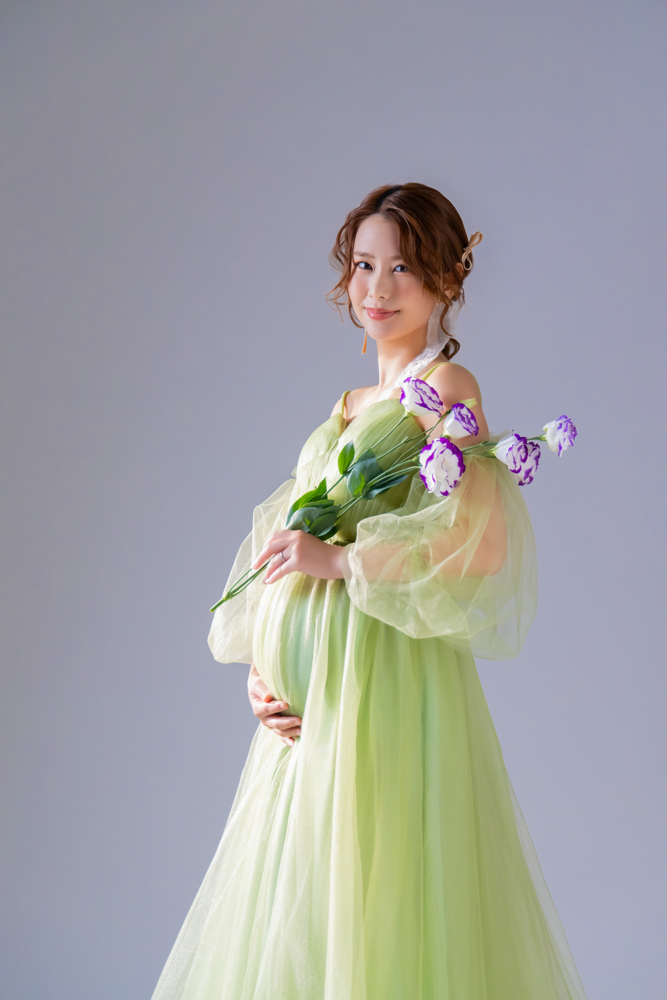 髪をまとめ、チューリップを手にしてグリーンのドレスをまとう姿