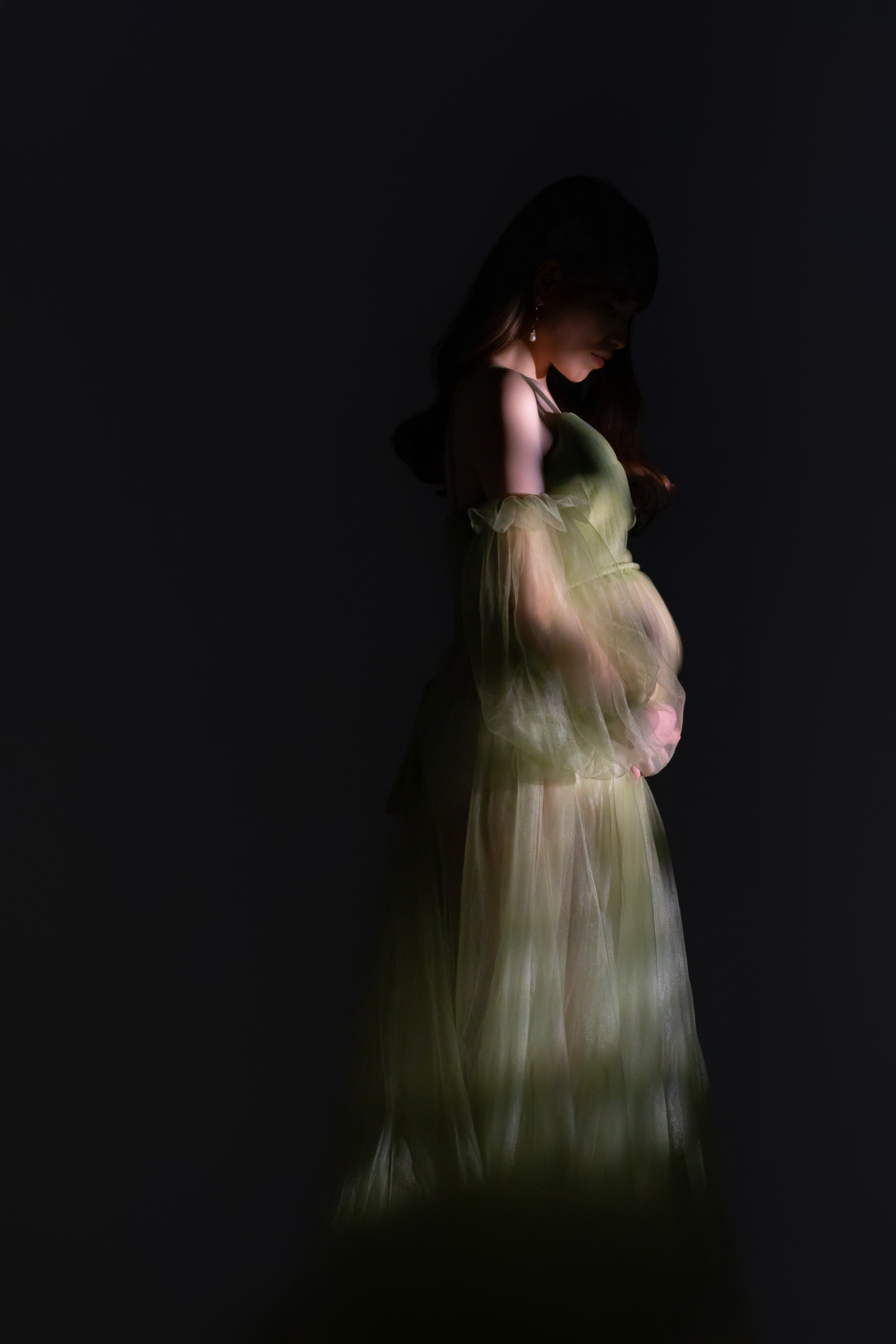 暗い背景の中、光を受けて立つグリーンのドレス姿
