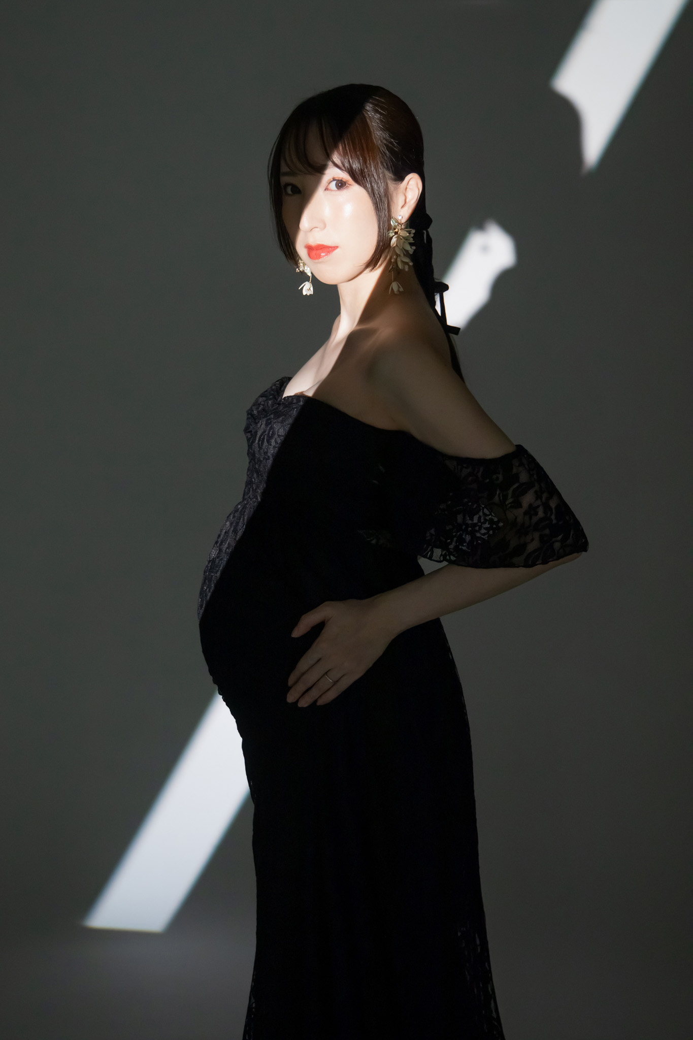 黒いレースのマタニティドレスをまとい、光と影の中に立つ姿