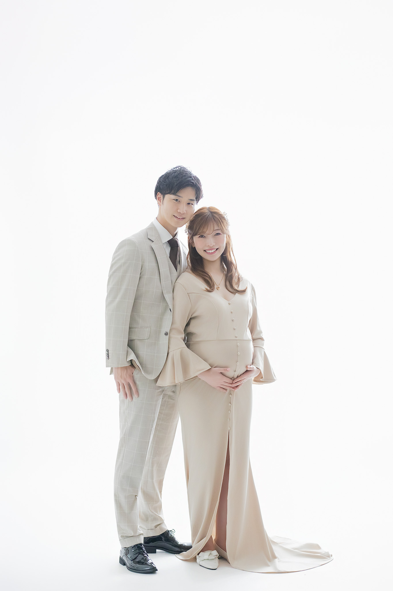 白い背景の前で向かい合い、お腹に手を添えるご夫婦