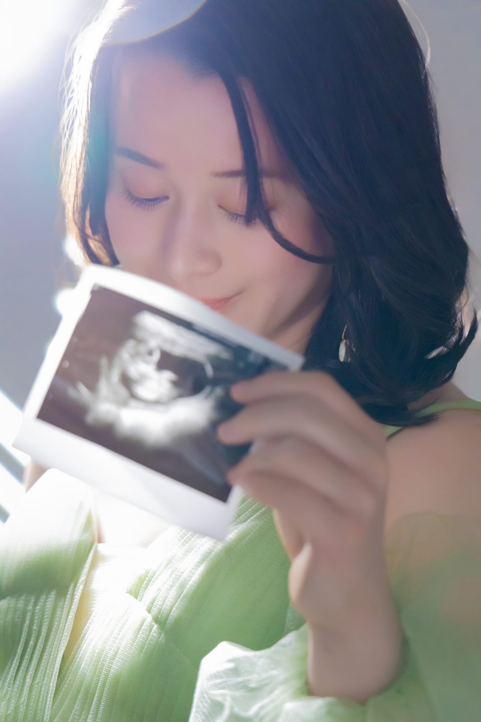 エコー写真をそっと胸元に寄せ、目を閉じる妊婦