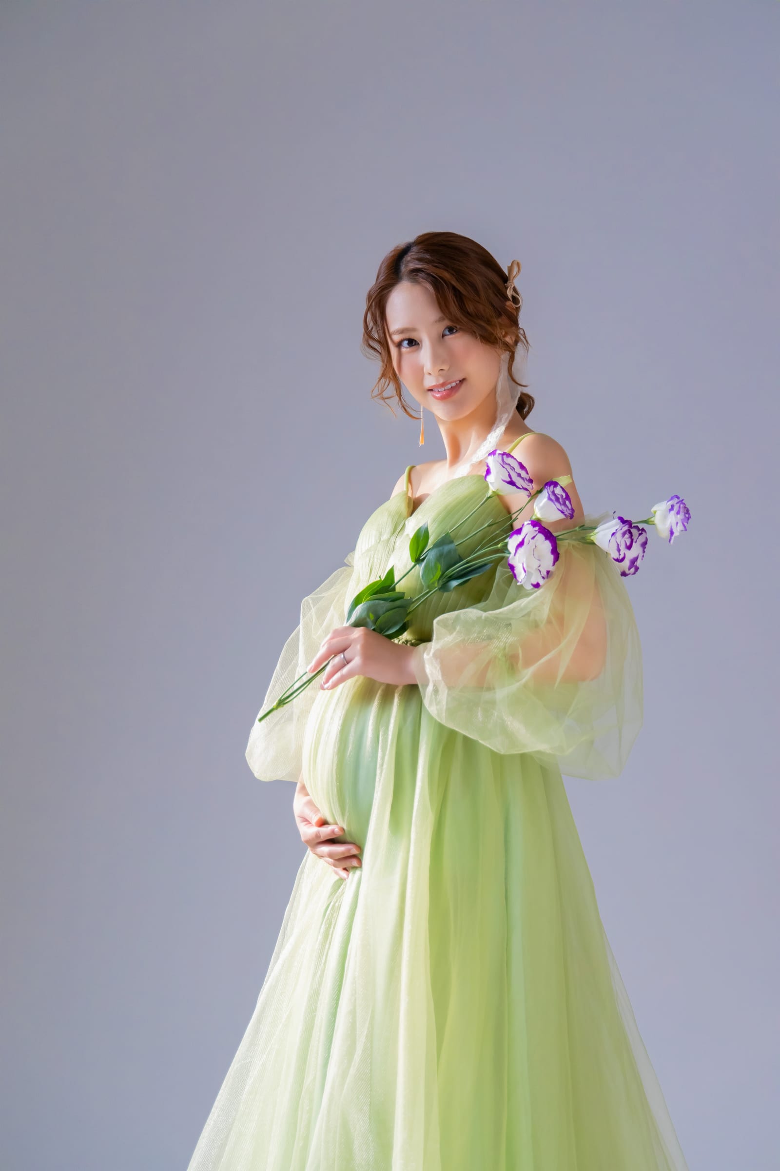 グリーンのチュールドレスで花束を抱える妊婦