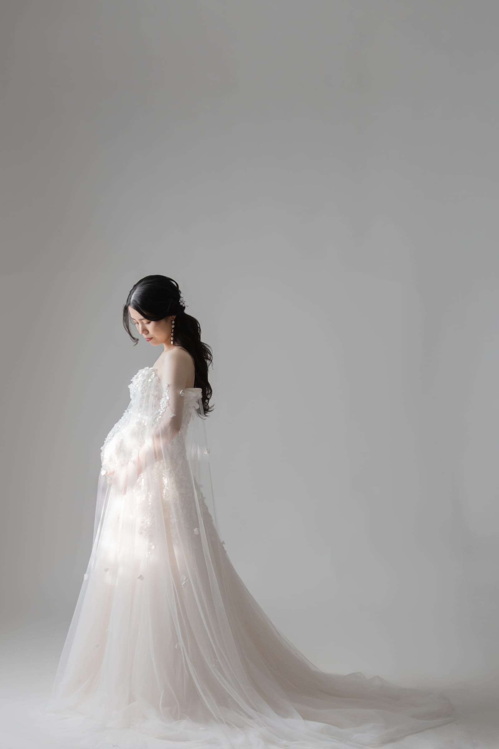 淡い光の中、白いドレスで静かに立つ妊婦