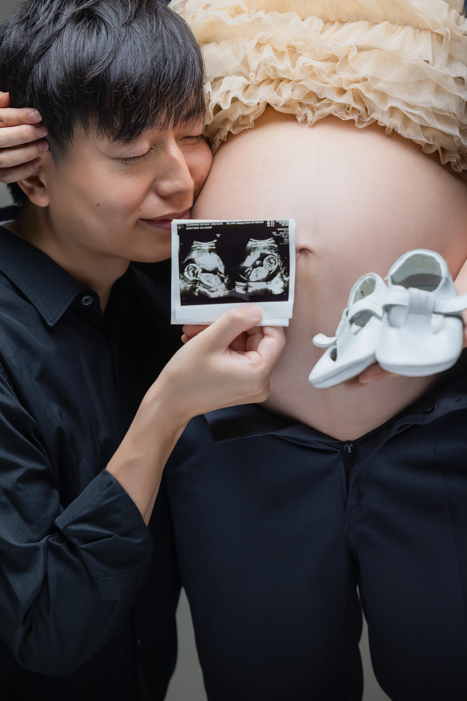 お腹に耳を寄せ、エコー写真とベビーシューズを持つご主人