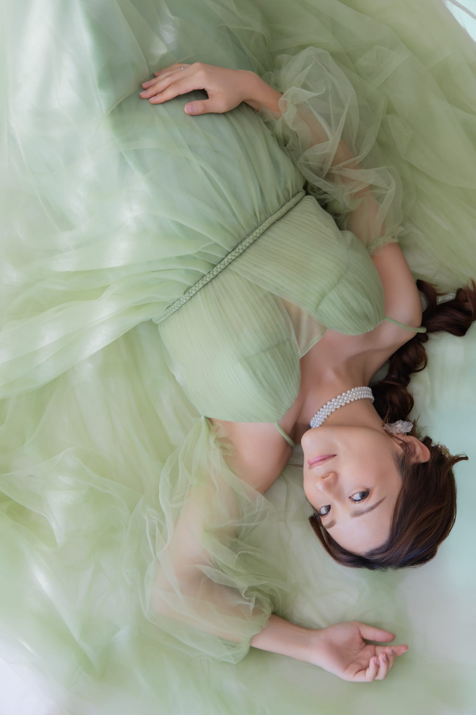 グリーンのドレスを広げ、床に横たわる妊婦