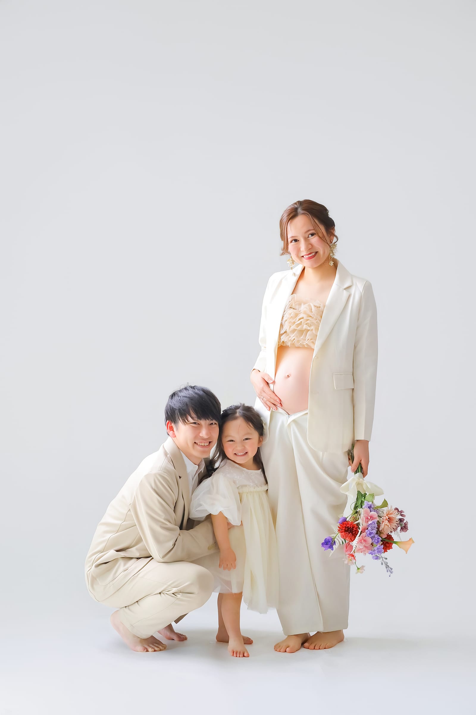 ベージュの装いで並ぶご夫婦と上の子の家族写真