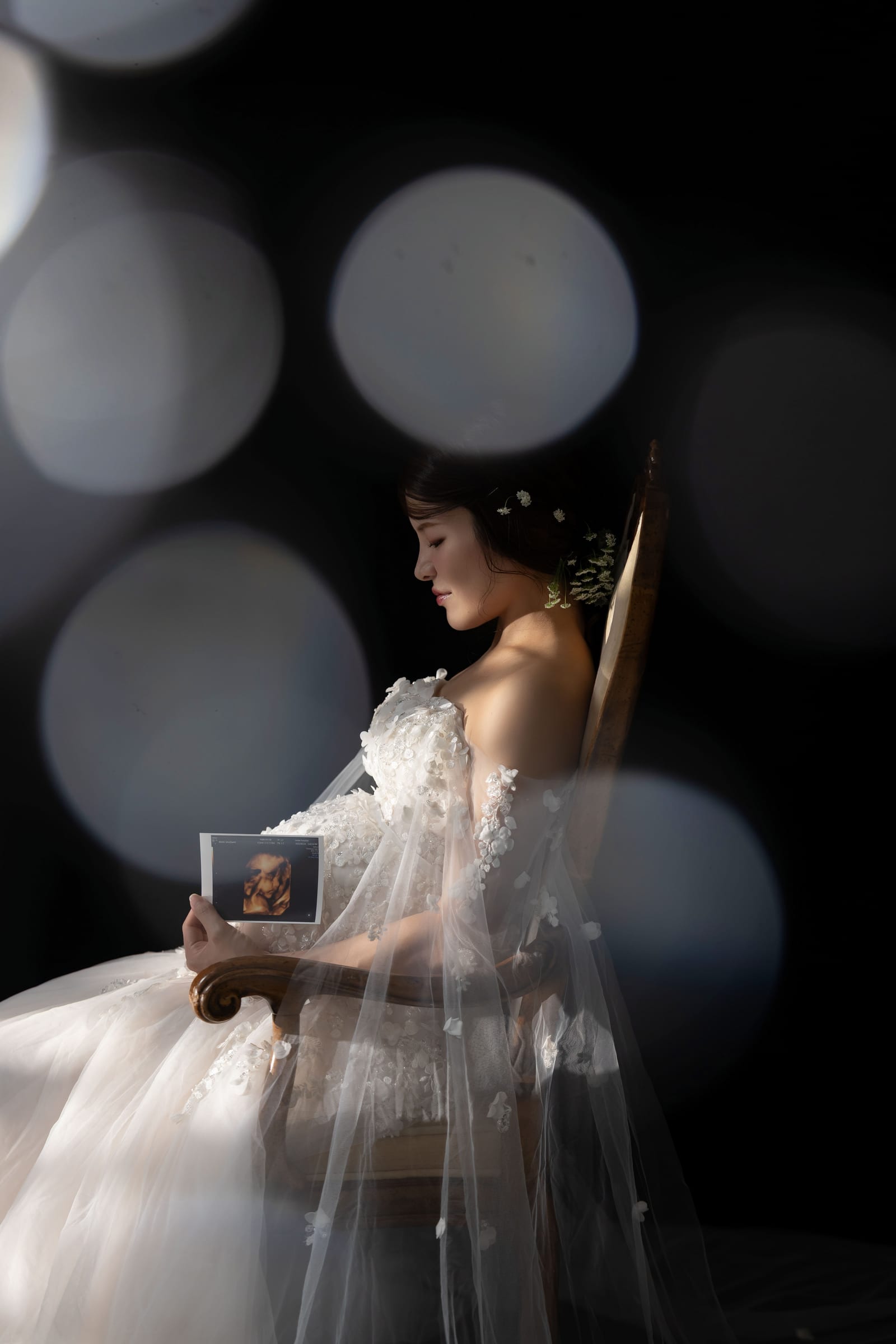 暗い背景に光の玉が浮かぶ中、エコー写真を持つ妊婦