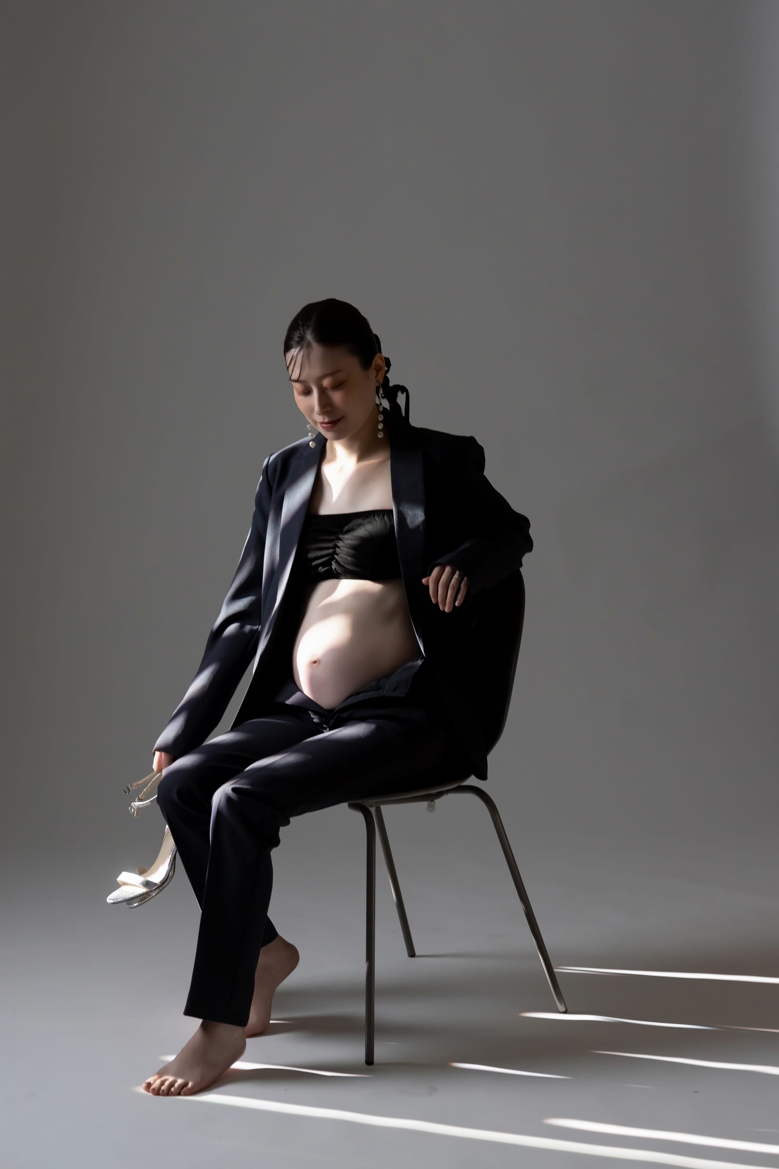 黒の装いで椅子に腰かけ、光と影の中に座る妊婦
