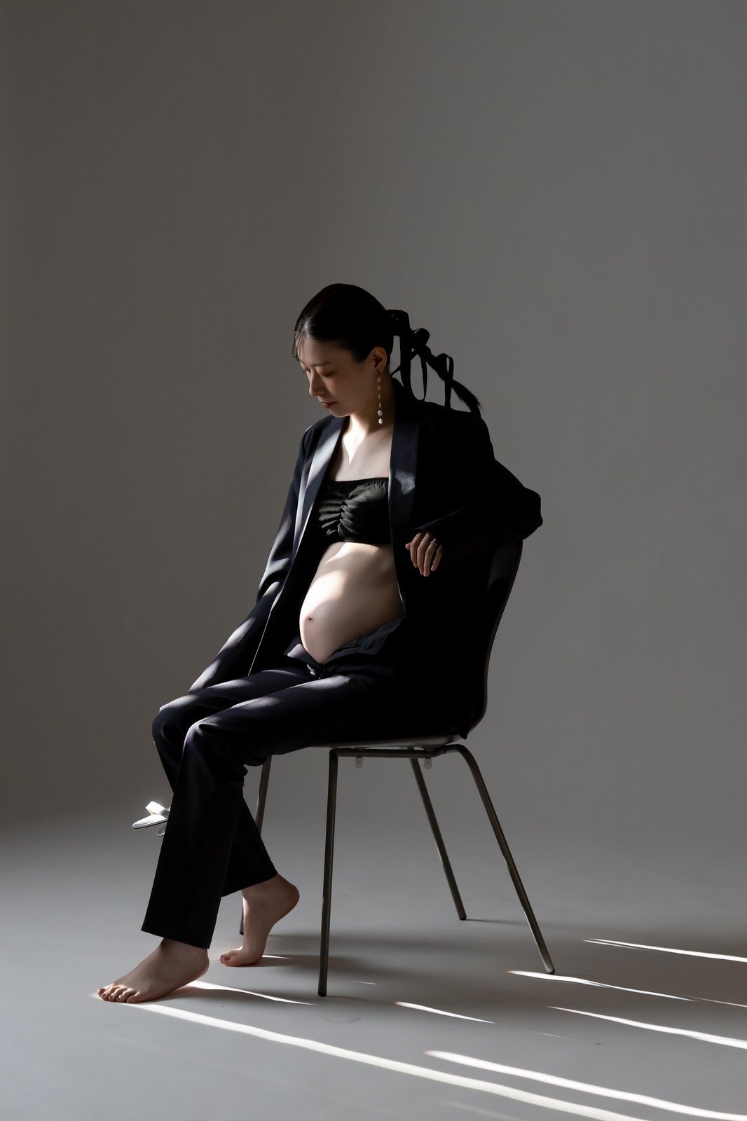 黒のセットアップ。椅子に腰掛けて、お腹に視線を落とす